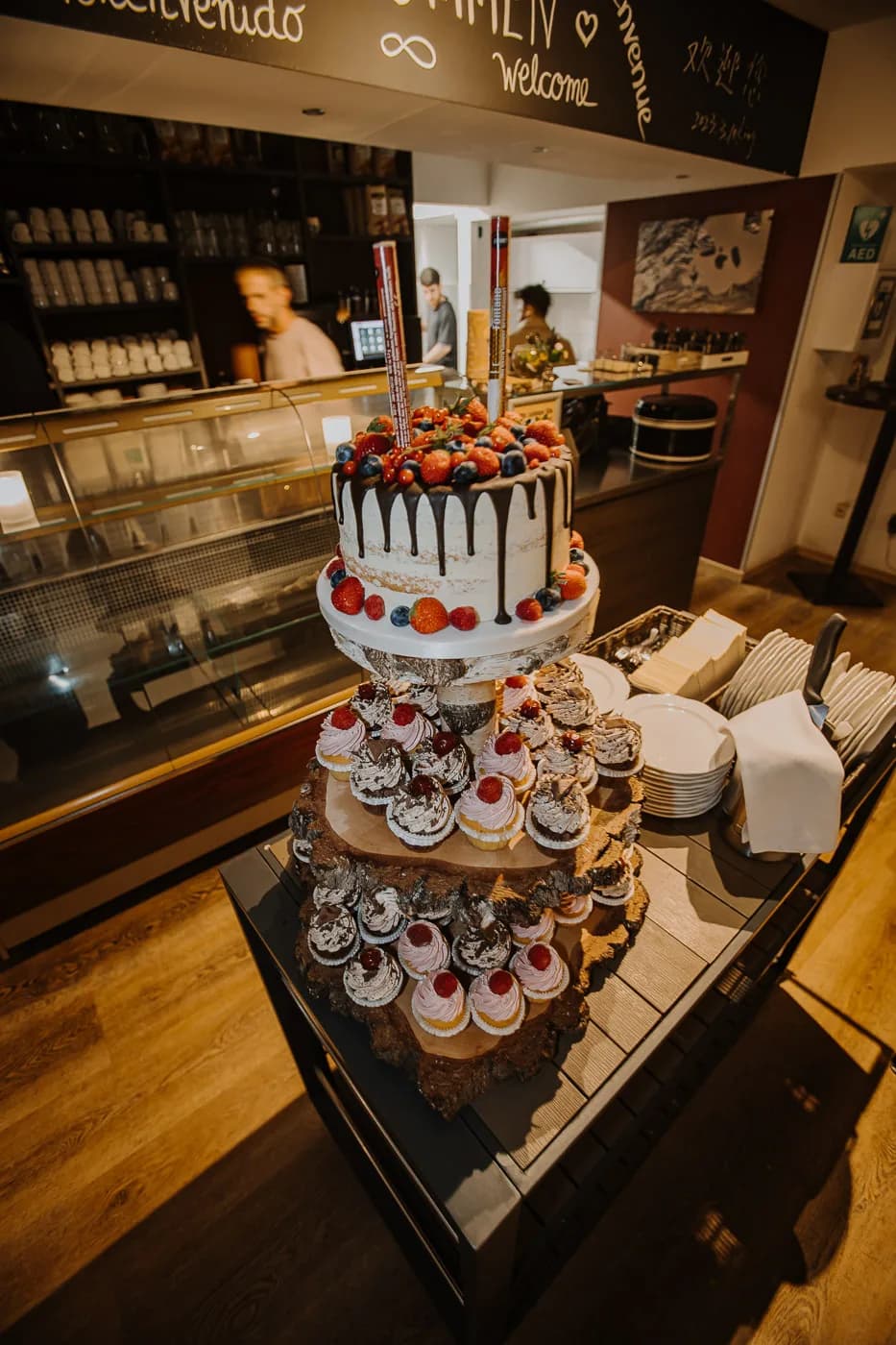 Dreistöckige Hochzeitstorte mit Beeren und Cupcakes auf rustikalem Holzstand