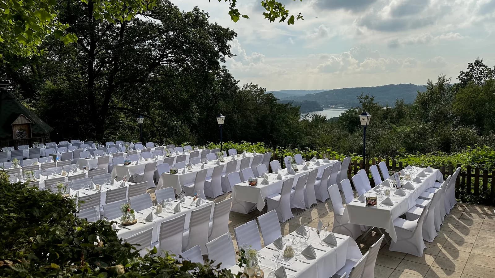 Lange Hochzeitstafel im Freien unter Sonnenschirmen mit Sitzplan und Blick auf das Ruhrtal