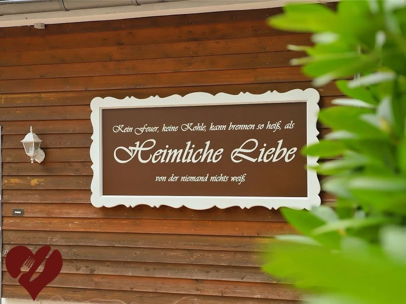 Historisches Holzschild „Heimliche Liebe — Kein Feuer, keine Kohle, kann brennen so heiß…“ an der hölzernen Hausfassade